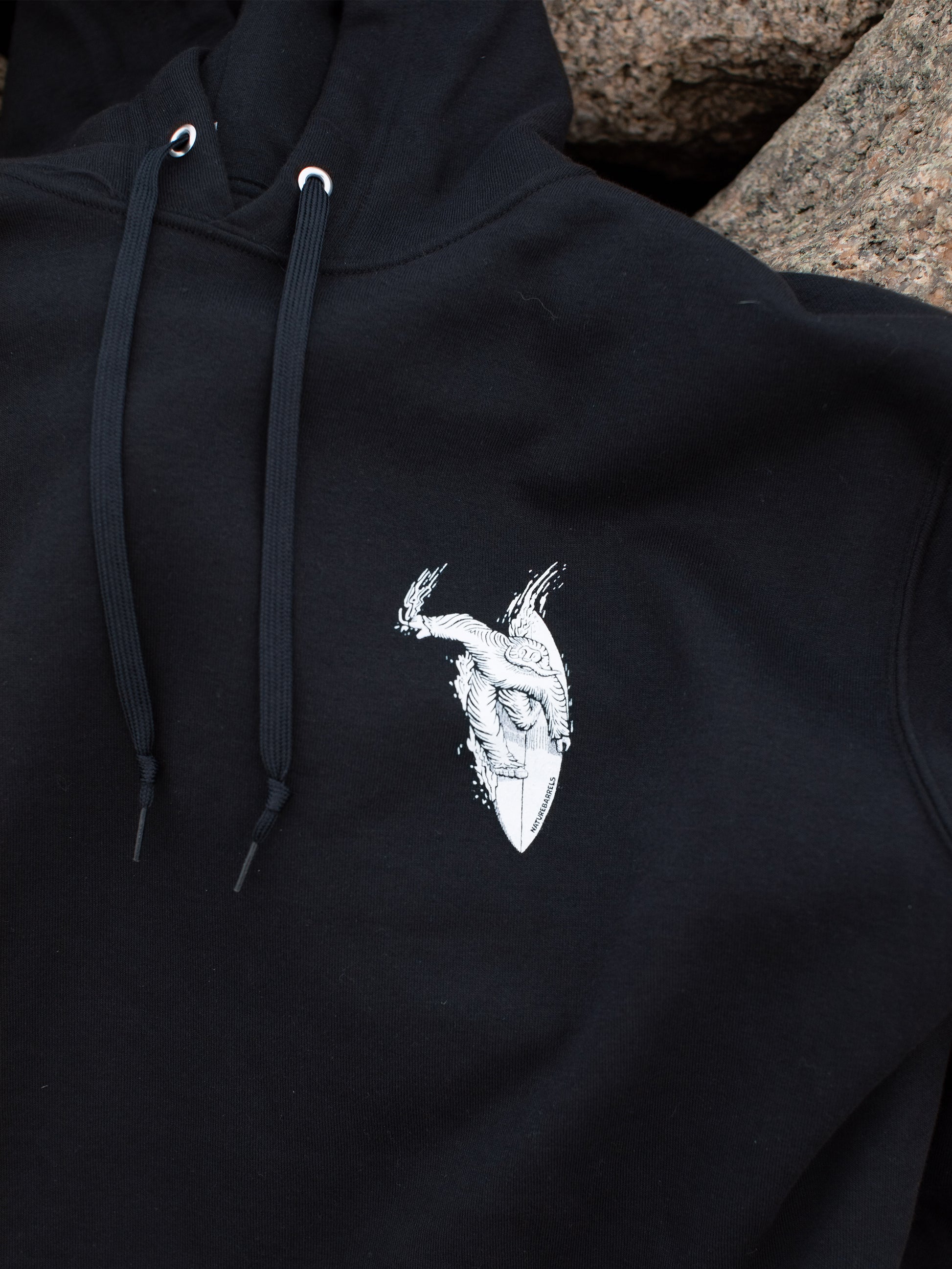 Close-up of a black hoodie with a small white chest graphic of a surfing sasquatch