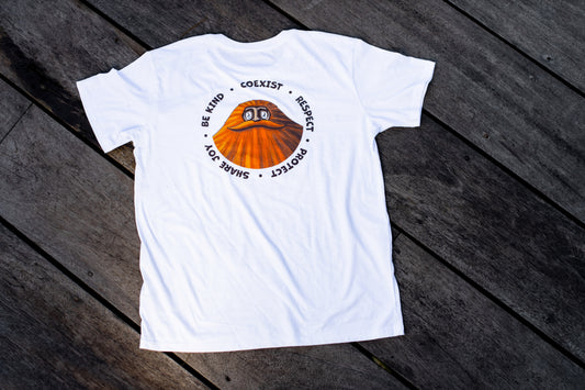 A white t-shirt with a central graphic of an orange sasquatch with a great moustache and the words 'Share Joy, Be Kind, Coexist, Respect, Protect' in a circular formation around the sasquatch portrait, lying flat on weathered wooden planks.